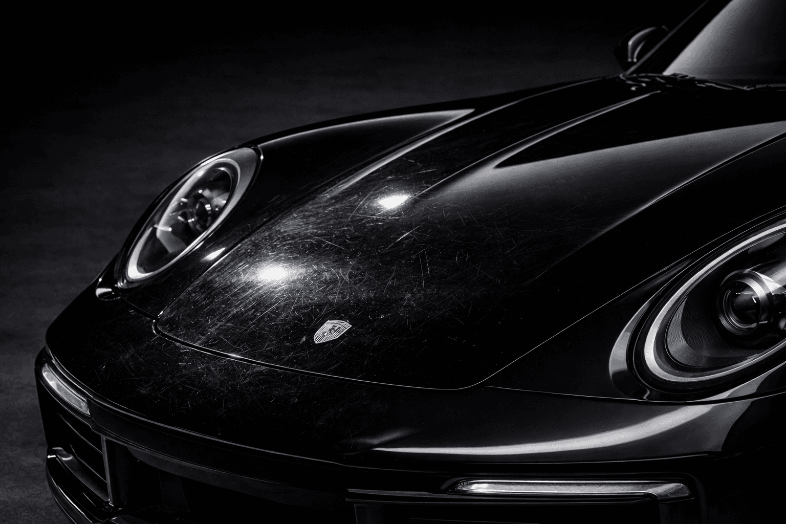 Close-up of a black car front panel showing visible swirl marks and surface scratches